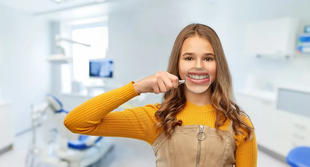 Girl Holding A Magnifier Next To Her White Teeth In A Dental Office