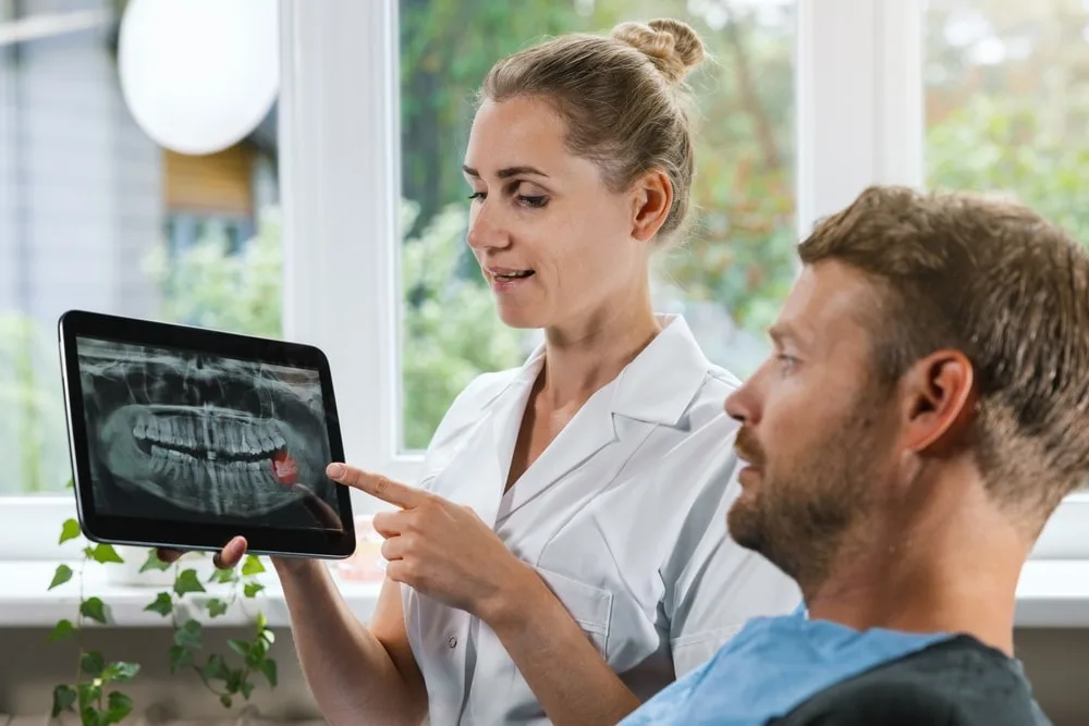 Dentist showing and explaining dental x-ray picture with impacted wisdom tooth to her patient.