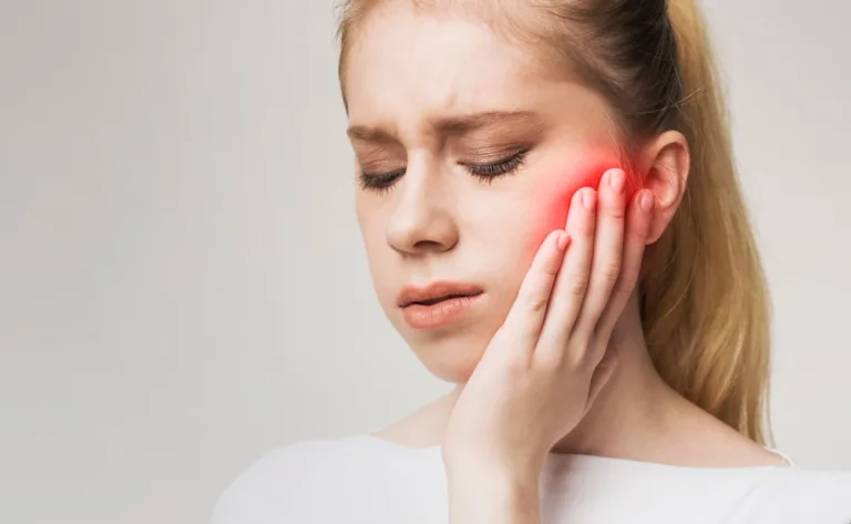 Young woman holding her cheek, suffering from jaw pain.