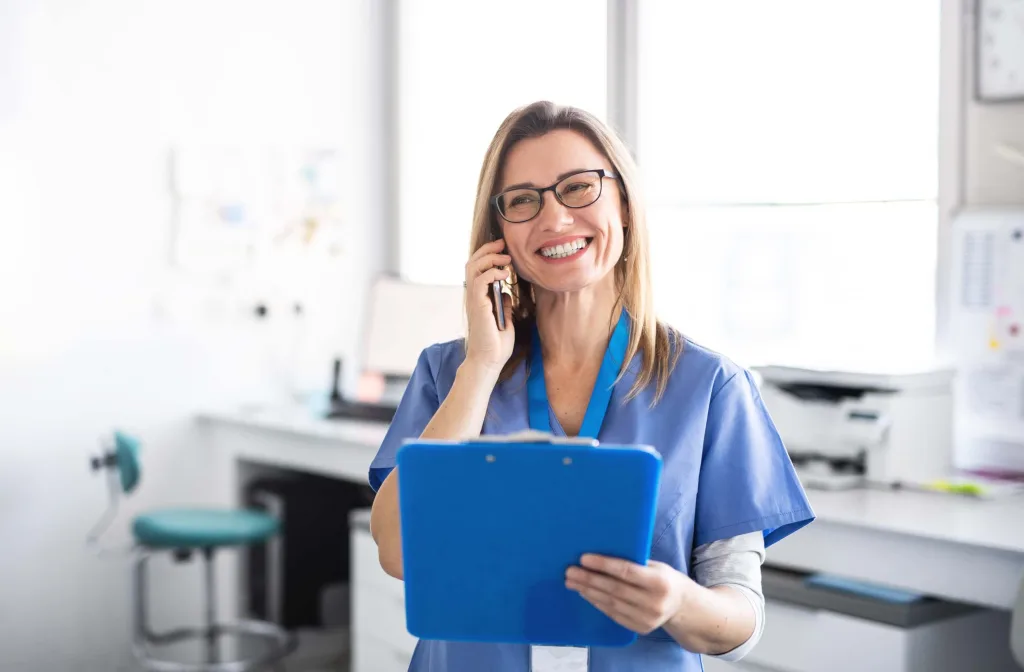 Portrait of dental assistant in modern dental surgery, using smartphone.