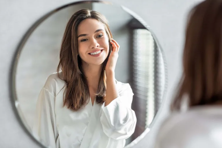 Beauty concept. Portrait of attractive happy woman looking at mirror in bathroom