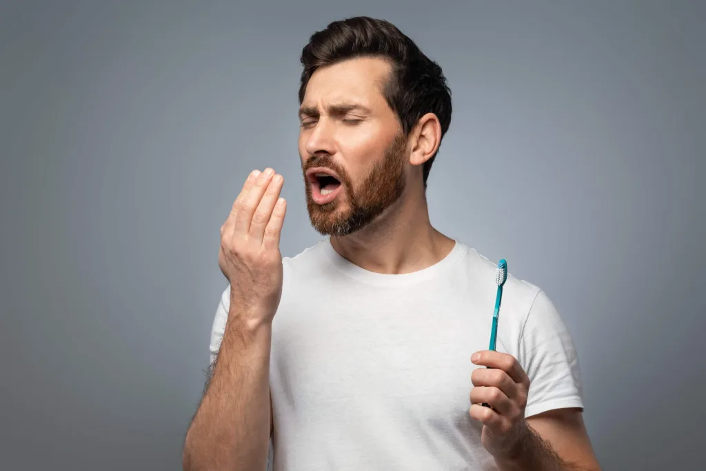 Bad breath. Handsome middle aged man checking his breath with hand