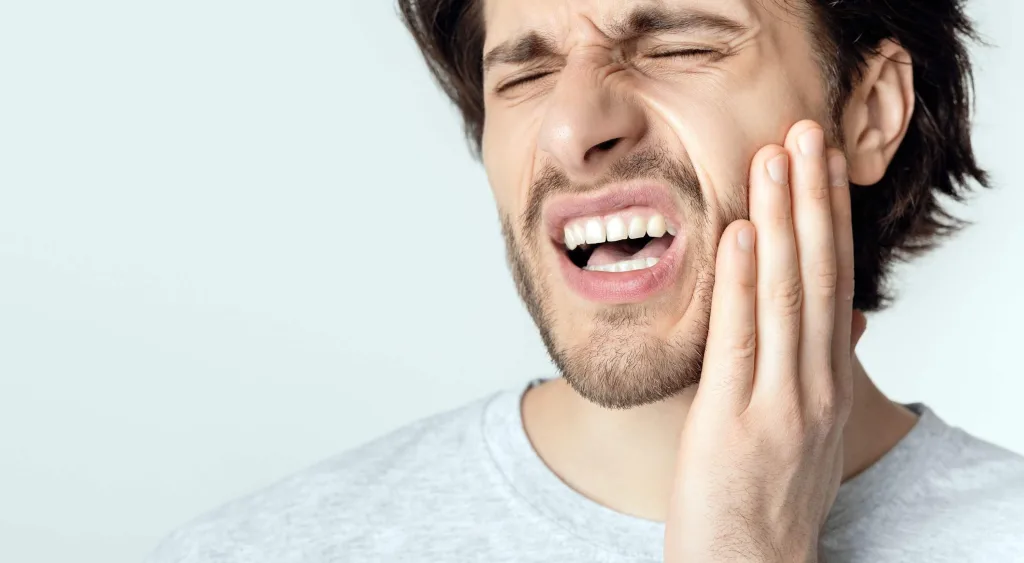 Young man feeling toothache, holding cheek with hand